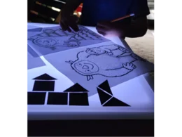 Person zeichnet ein Monster auf einem Leuchttisch mit Bleistift nach.