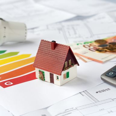 Ein Modellhaus liegt auf einem Energieausweis, Bauplänen und Geldscheinen.
