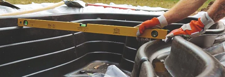 Person misst Teich mit Wasserwaage aus