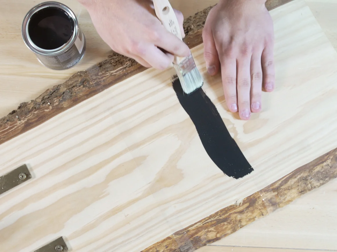 Person streicht Holzbrett mit Pinsel schwarz an