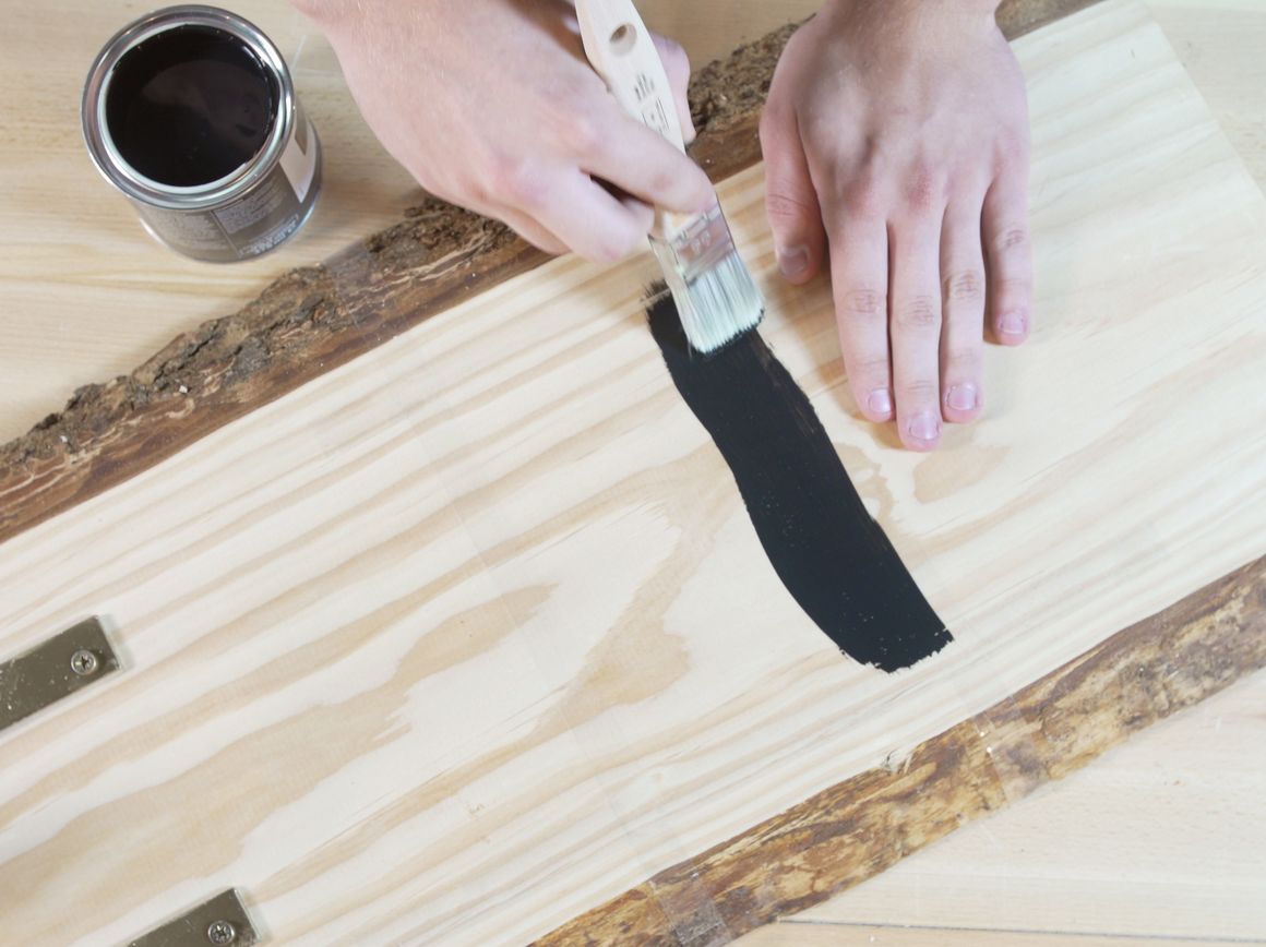 Person streicht Holzbrett mit Pinsel schwarz an
