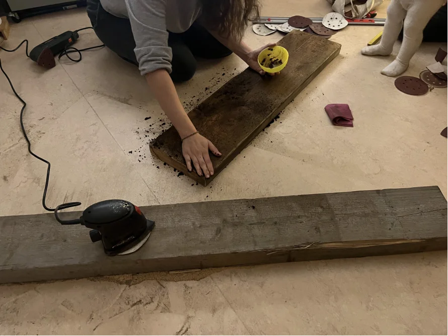 Person schleift Holzbrett mit Schleifmaschine