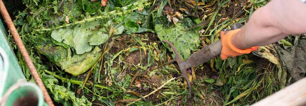 Eine Person wendet mit einer Gabel den Kompost in einem Komposter um.