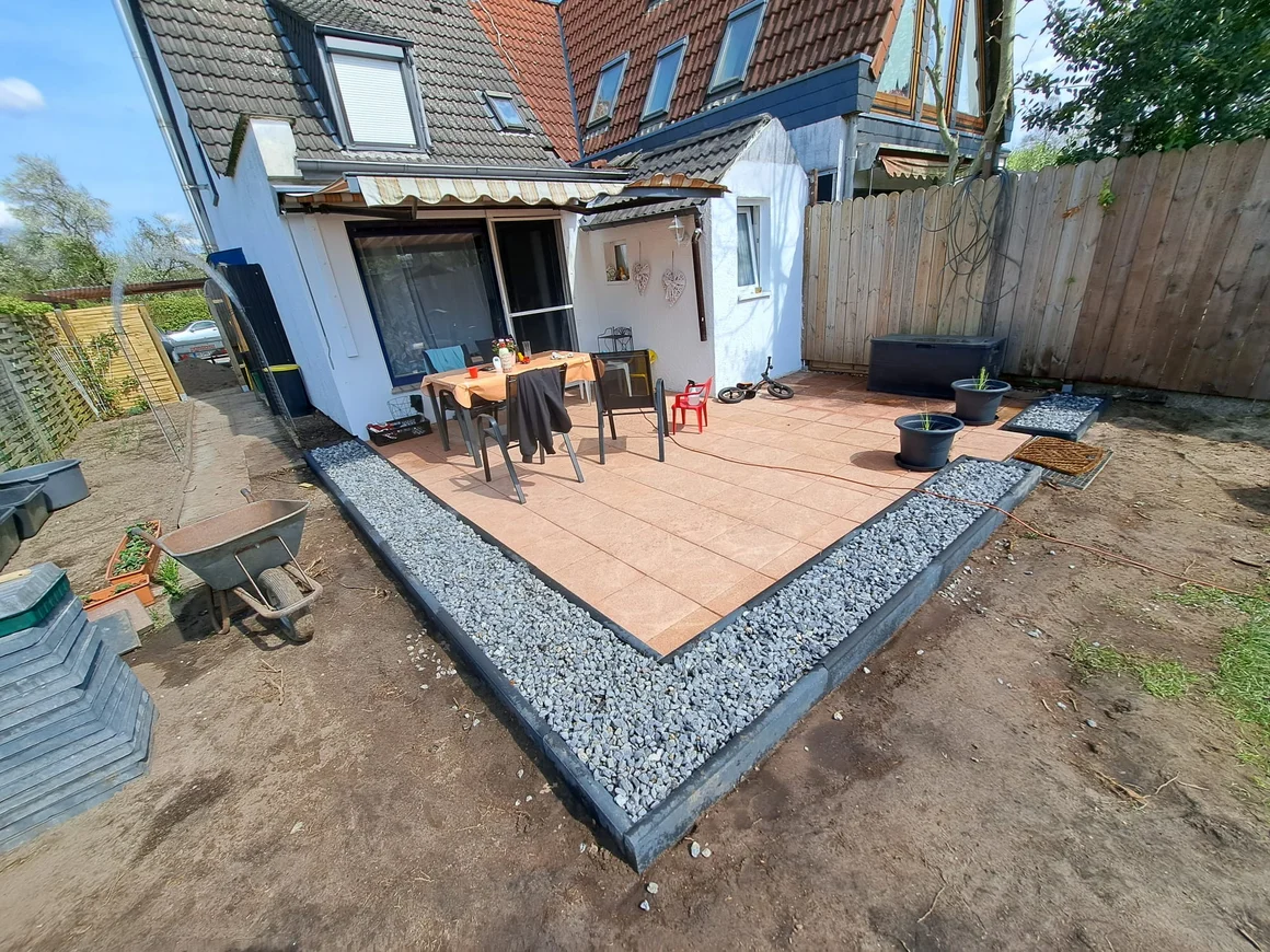 Eine neu angelegte Terrasse im Garten mit einer Schubkarre daneben.