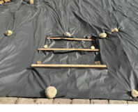 Schwarze Folie mit drei Holzlatten und Steinen