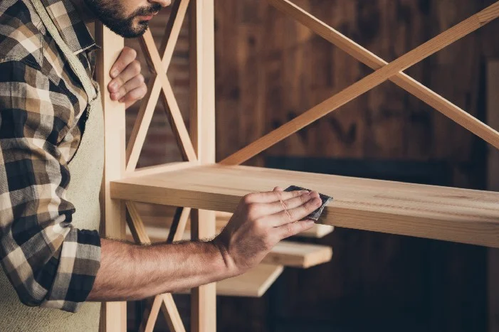 Person schleift Holzbrett mit Schleifpapier