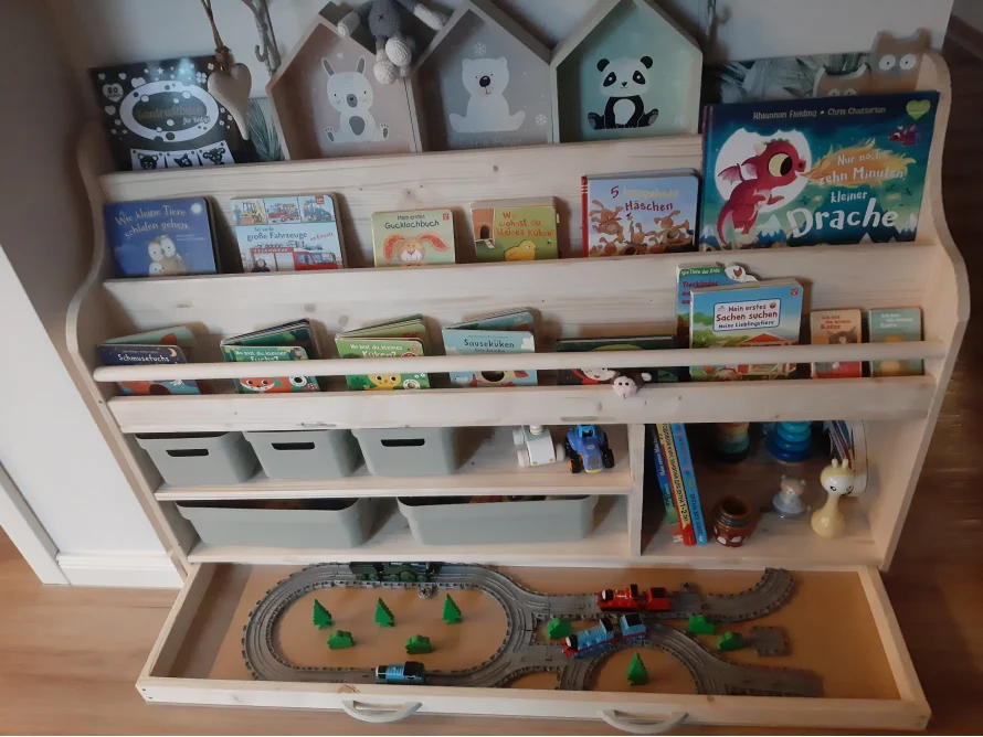 Ein weißes Bücherregal aus Holz mit Spielzeug und Büchern.