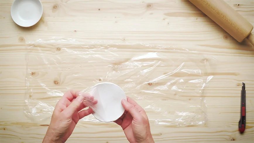 Hände wickeln Frischhaltefolie um einen Teller