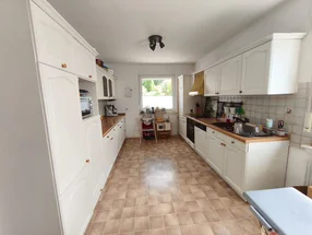 Lange, schmale Küche mit weißen Schränken und braunen Fliesenboden.