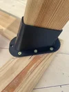 Ein Holzpfosten wird mit einer schwarzen Halterung und Schrauben an einem Holzbalken befestigt.