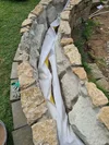 Eine im Bau befindliche Steinmauer mit einem gelben Drainagerohr.