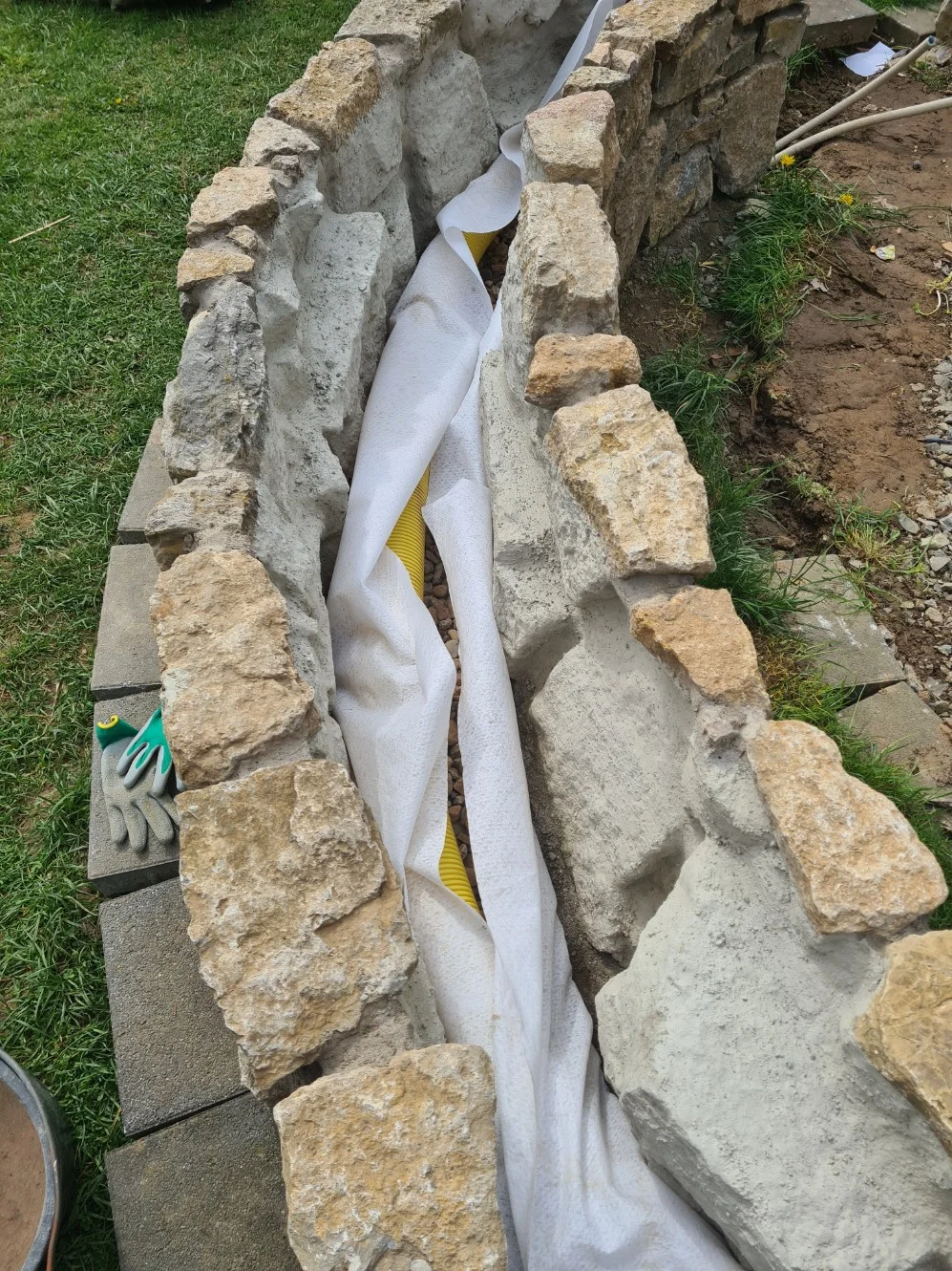 Eine im Bau befindliche Steinmauer mit einem gelben Drainagerohr.