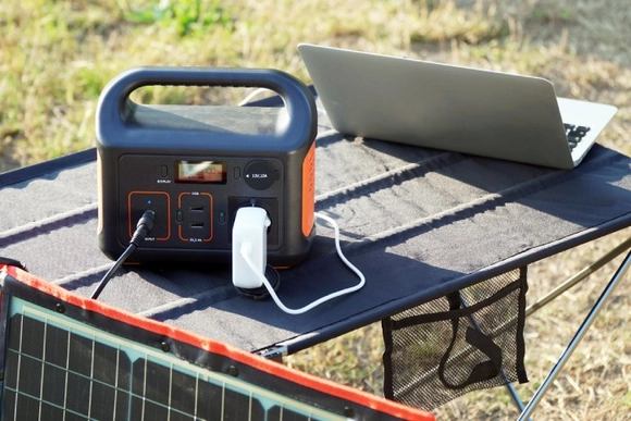 Eine Powerstation wird von einem Solarmodul geladen und versorgt einen Laptop.