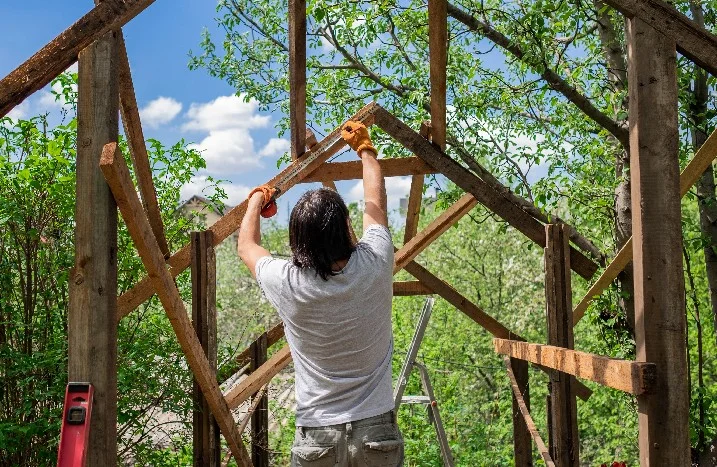 Person baut ein Gartenhaus aus Holz.