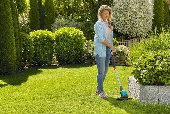 Eine Person trimmt mit einem Rasentrimmer die Rasenkante in einem Garten.