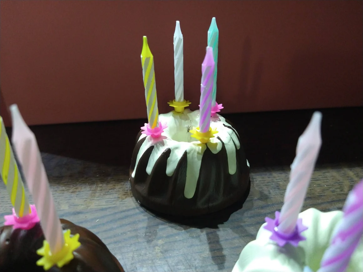 Ein kleiner Schokoladen-Gugelhupf mit weißem Zuckerguss und bunten Geburtstagskerzen.