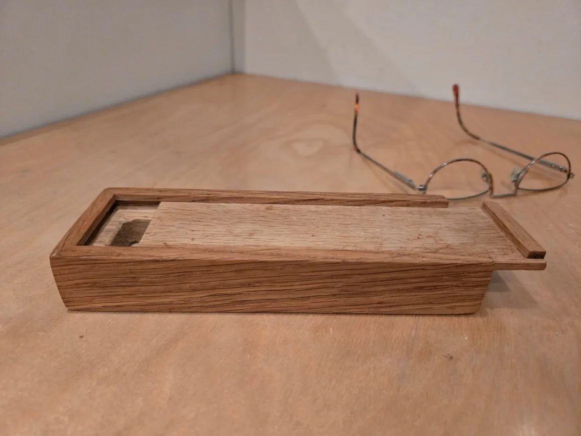 Eine kleine Box aus Holz liegt neben einer Brille.
