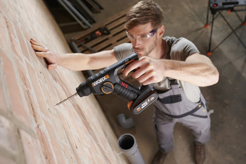 Person bohrt mit Bohrhammer in Ziegelwand