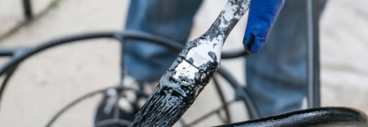 Hand mit Pinsel trägt schwarze Farbe auf Metallstuhl auf
