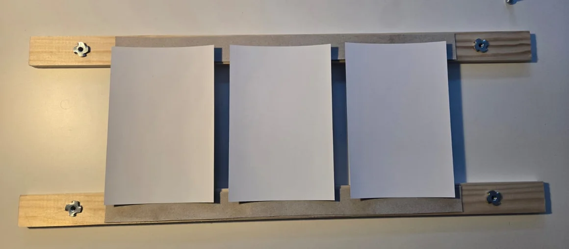 Eine hölzerne Pflanzenpresse mit drei weißen Blättern Papier.