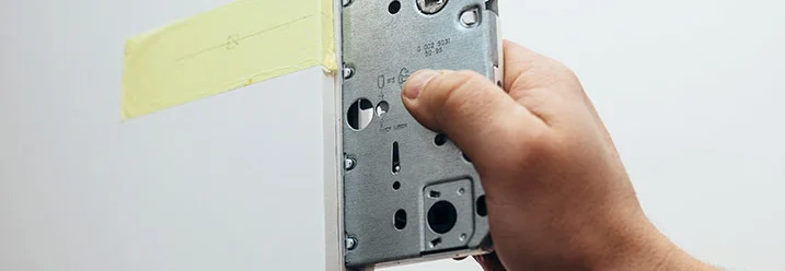 Person hält ein Türschloss an eine Tür.