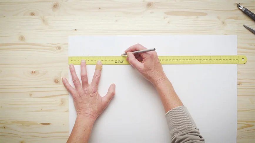 Zwei Hände zeichnen mit einem Bleistift und einem Lineal eine Linie auf ein Blatt Papier