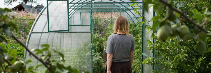 Person mit Gießkanne vor Gewächshaus