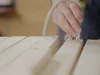 Person fädelt Seil durch Holzlatten