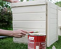 Person streicht Gartenhaus mit Pinsel