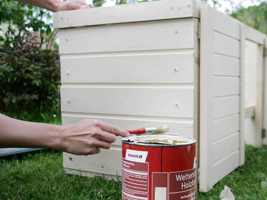 Person streicht Gartenhaus mit Pinsel