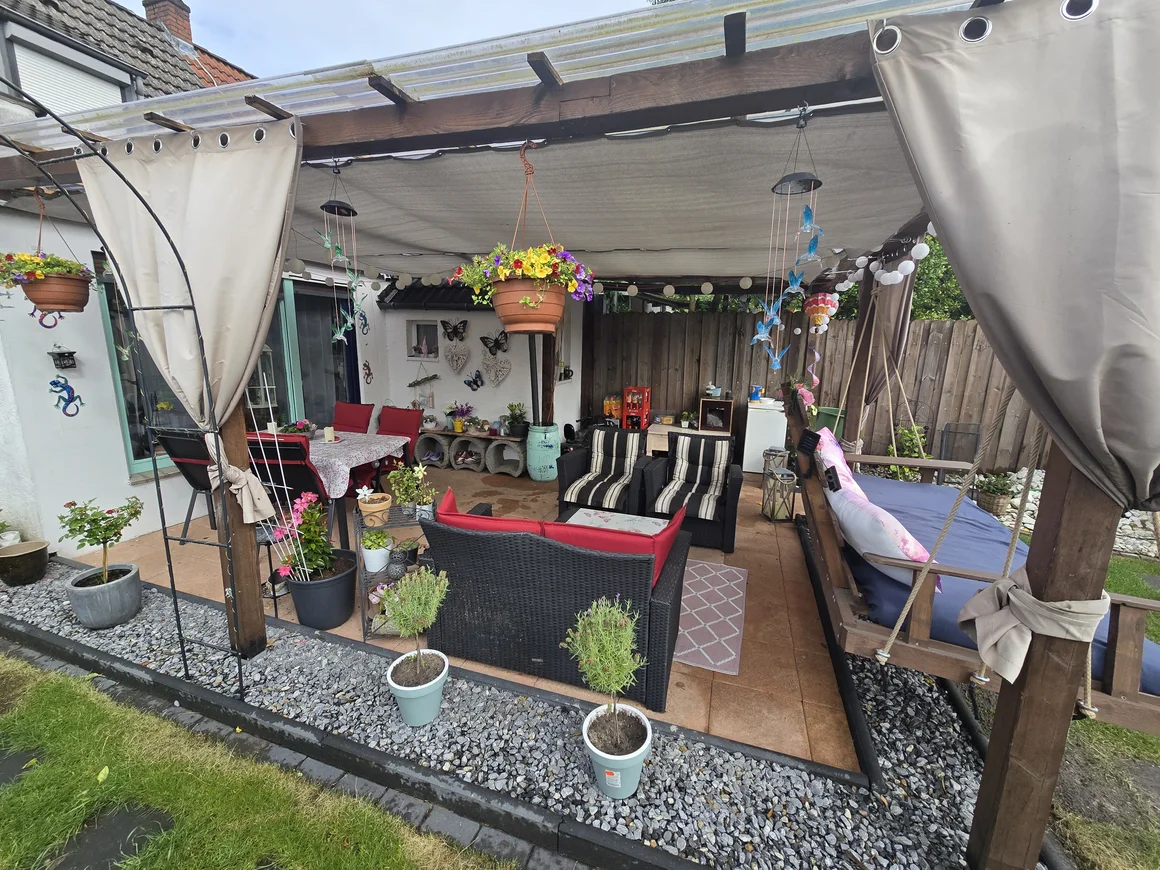Eine gemütlich eingerichtete Terrasse mit vielen Pflanzen und Sitzmöbeln.