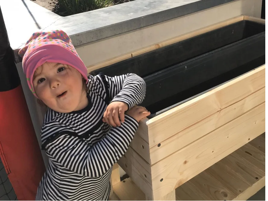Kleinkind mit Mütze lehnt an Hochbeet