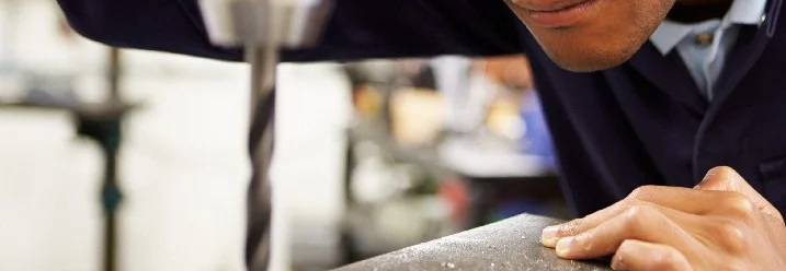 Person bohrt mit einer Standbohrmaschine in Metall