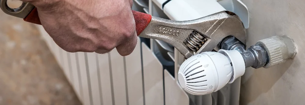 Person montiert Heizkörperthermostat mit Schraubenschlüssel.