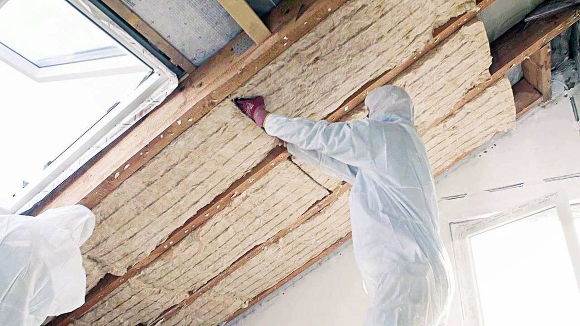 Ein Handwerker bringt die Dachdämmung zwischen den Sparren an.