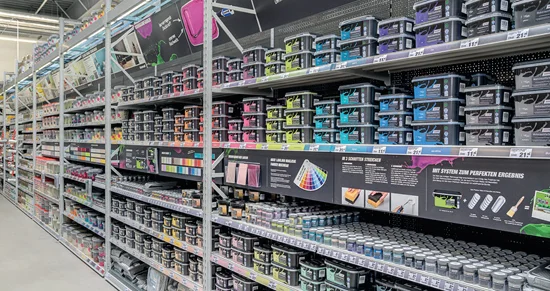 Ein langer Gang in einem Baumarkt mit Regalen voller verschiedener Farbeimer.