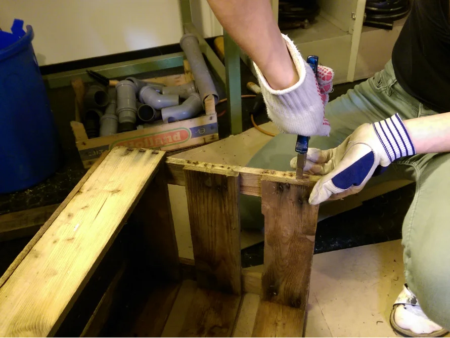 Person baut mit Cuttermesser Holzkiste zusammen