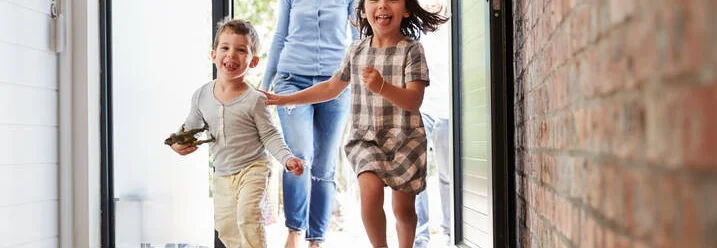 Drei Kinder rennen lachend aus dem Haus.