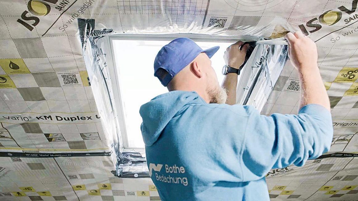 Ein Handwerker bringt zum Dachfenster dämmen Dampfbremsfolie rund um das Fenster an.