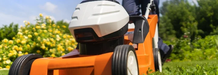 Person mäht Rasen mit Rasenmäher.