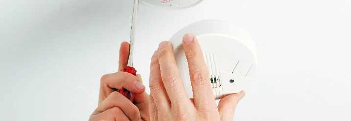 Person montiert Rauchmelder an Decke