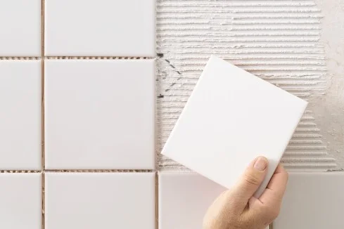 Hand verlegt eine Fliese an eine Wand.