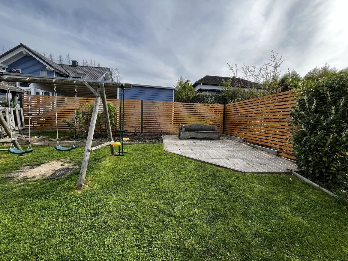 Ein Garten mit einem Schaukelgerüst, einer Bank und einem Holzzaun.