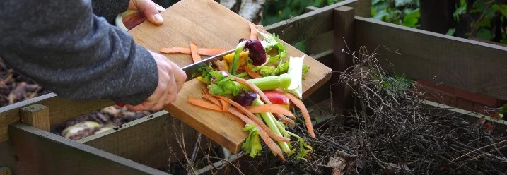 Person gibt Gemüseabfälle mit Messer in Komposter