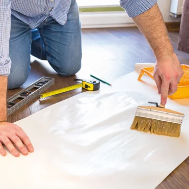 Person trägt Kleister mit Pinsel auf Tapete auf