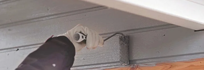 Person streicht Holzfassade grau
