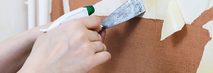 Person entfernt Tapete mit Spachtel