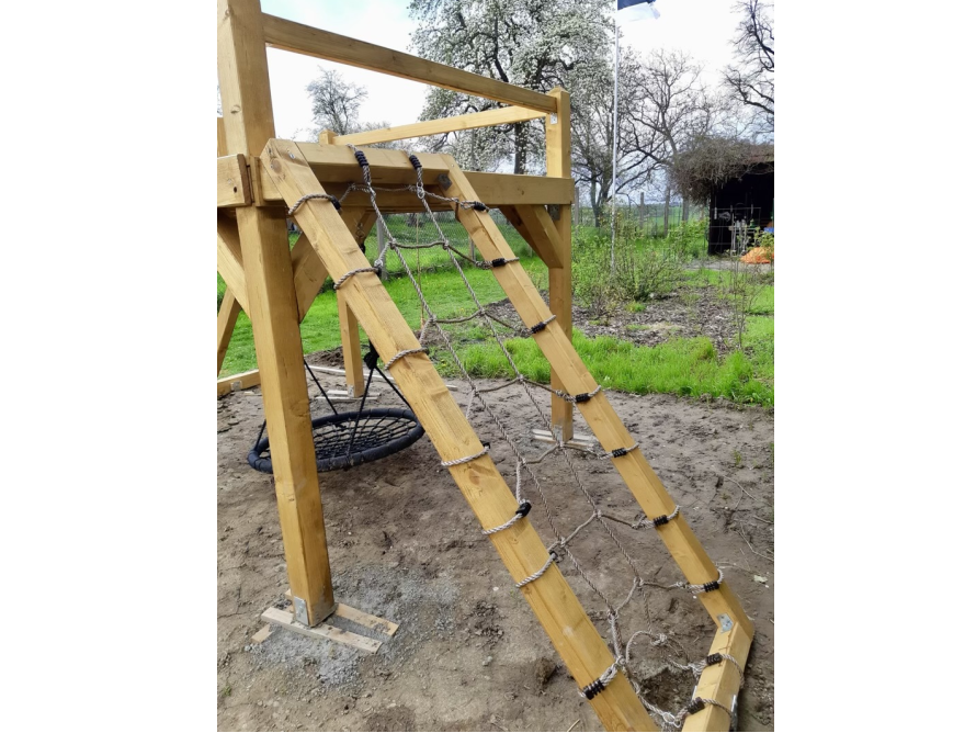 Ein Spielturm aus Holz mit Kletternetz und Nestschaukel.