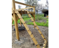 Ein Spielturm aus Holz mit Kletternetz und Nestschaukel.