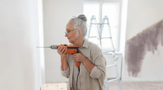 Person mit Gehörschutz bohrt mit Bohrmaschine in Holz